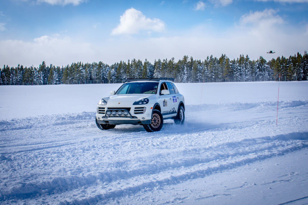 White SUV driving on a snow-covered track with trees in the background