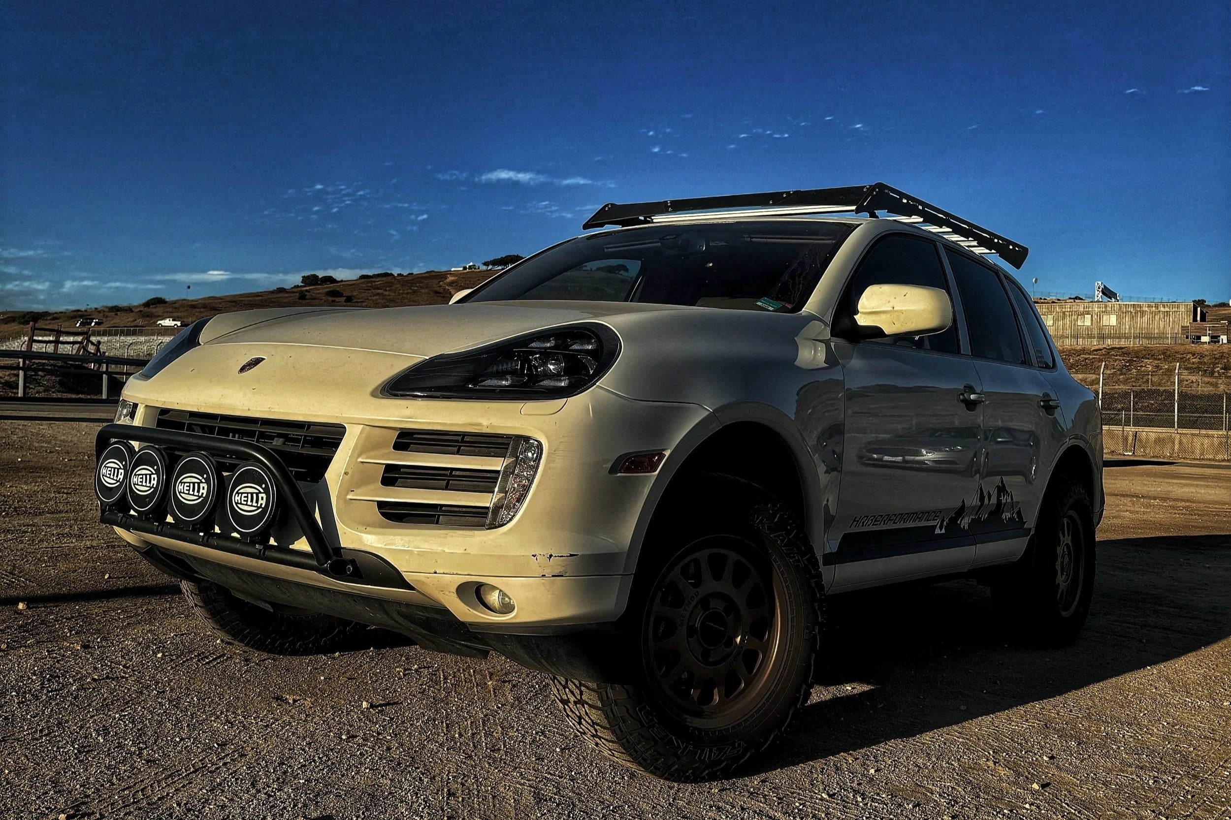 Porsche Cayenne 957 with off-road modifications on a gravel surface under a clear blue sky. Showing the mountain side graphic for HRBerformance