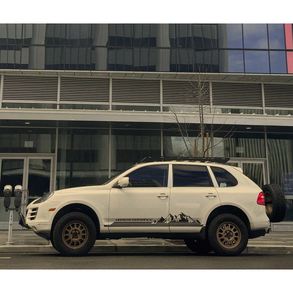 White Porsche Cayenne 957 with off-road modifications parked in front of a modern building, with the HRBerformance side graphic