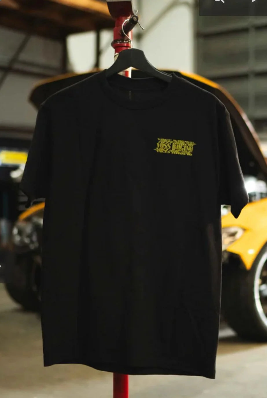 Voss Racing Black t-shirt with yellow logo on a hanger against a blurred background